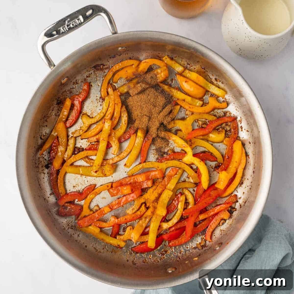 The remaining jerk seasoning and turmeric powder are stirred into the sautéed bell peppers, infusing them with aromatic spices.