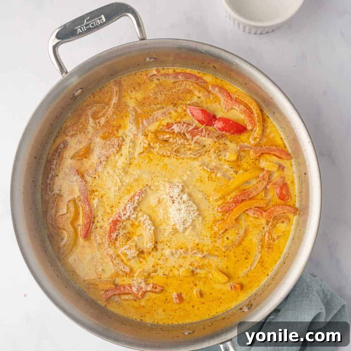 A rich, spicy cream sauce simmering gently in a skillet, blending chicken stock, heavy cream, and jerk seasoning.