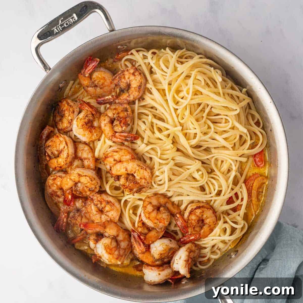 Cooked linguine pasta and tender shrimp are gracefully tossed with the vibrant, creamy Rasta Pasta sauce in a large skillet.