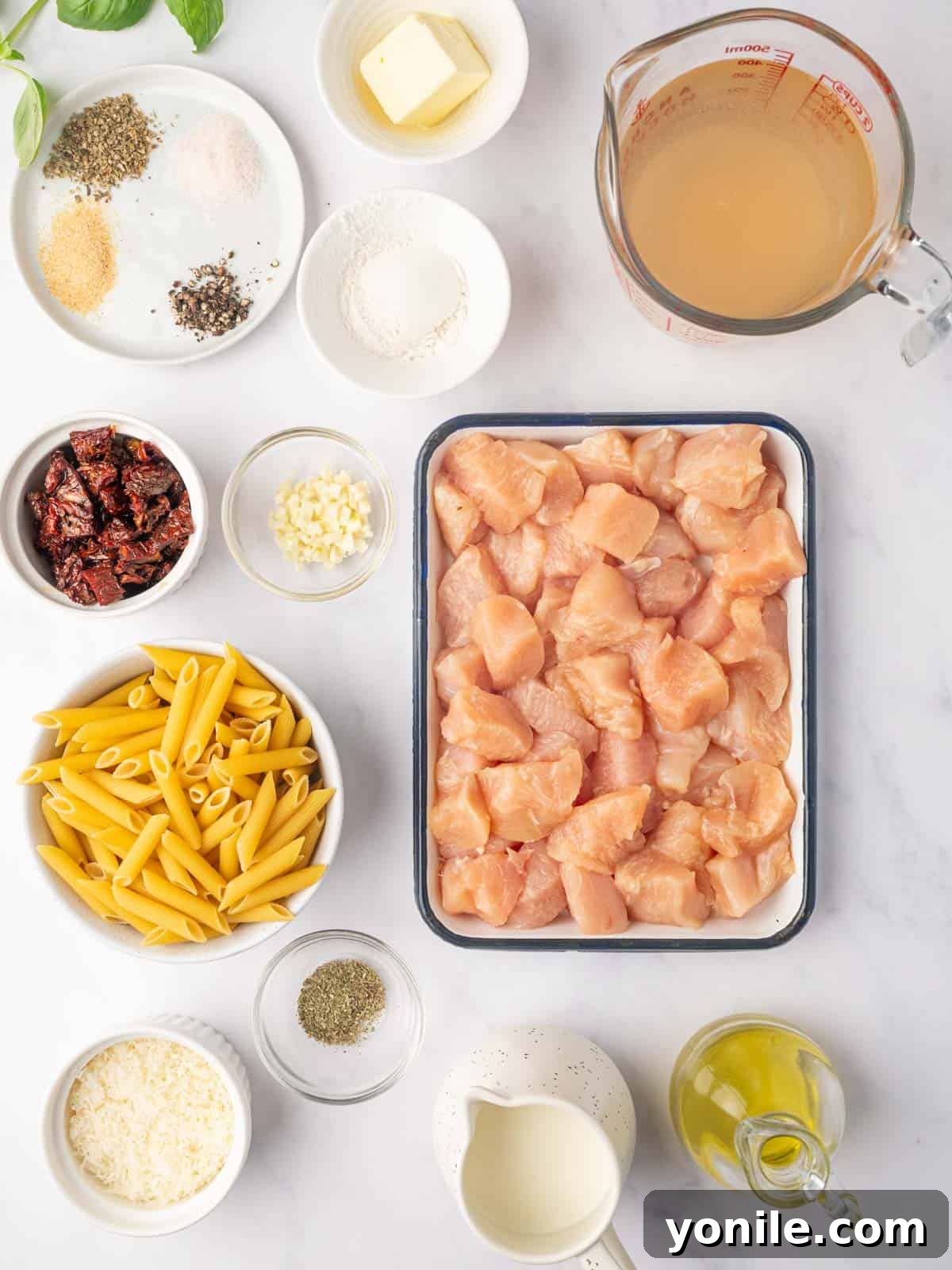 Proposal Chicken Pasta 3 A display of fresh ingredients laid out for marry me chicken pasta, including chicken, penne pasta, sun-dried tomatoes, and herbs.