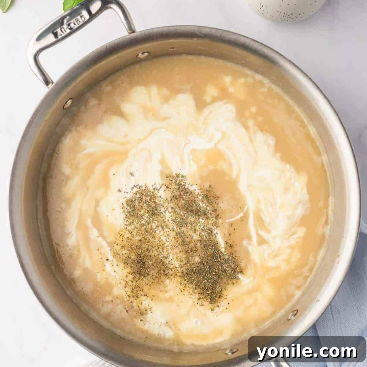 Proposal Chicken Pasta 7 Creamy sauce simmering in a skillet, with chicken broth and heavy cream being incorporated.