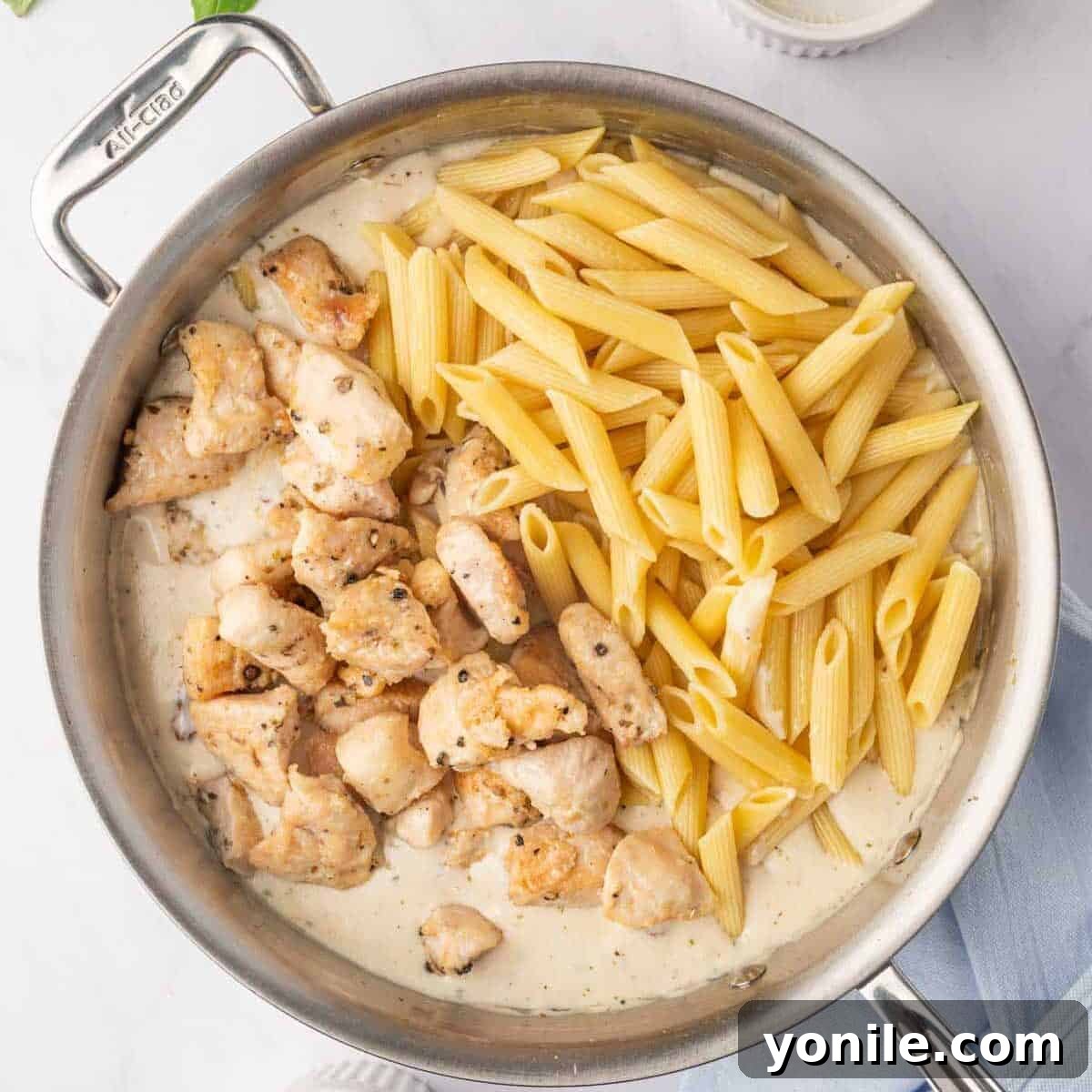 Proposal Chicken Pasta 9 Cooked penne pasta, chicken, and creamy sauce combined in a skillet, ready to be tossed together.