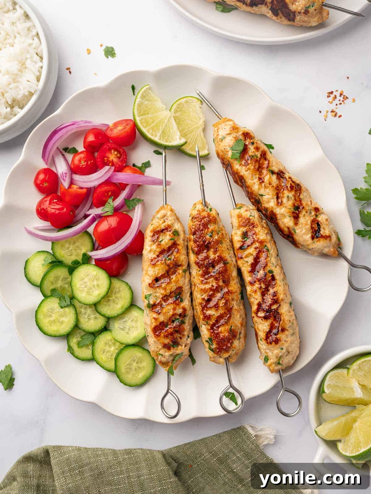 Flavorful Chicken Kofta Skewers 2 A beautifully arranged platter of golden-brown grilled chicken kofta skewers alongside vibrant roasted vegetables and fresh lime wedges.