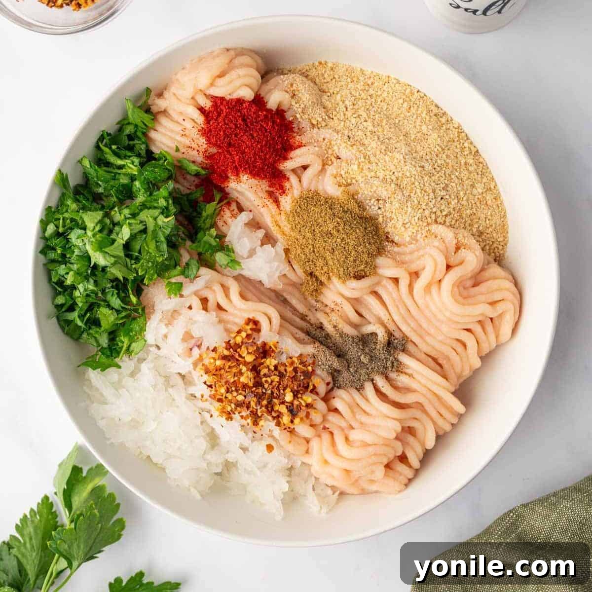 Flavorful Chicken Kofta Skewers 4 Close-up of ground chicken being mixed with finely chopped herbs and various spices in a large bowl, highlighting the vibrant colors of the ingredients.