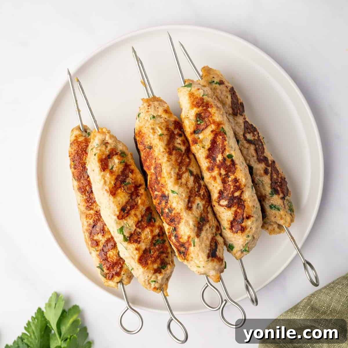 Flavorful Chicken Kofta Skewers 7 Freshly grilled chicken kofta skewers, perfectly charred with grill marks, arranged on a serving platter with a garnish of fresh herbs.