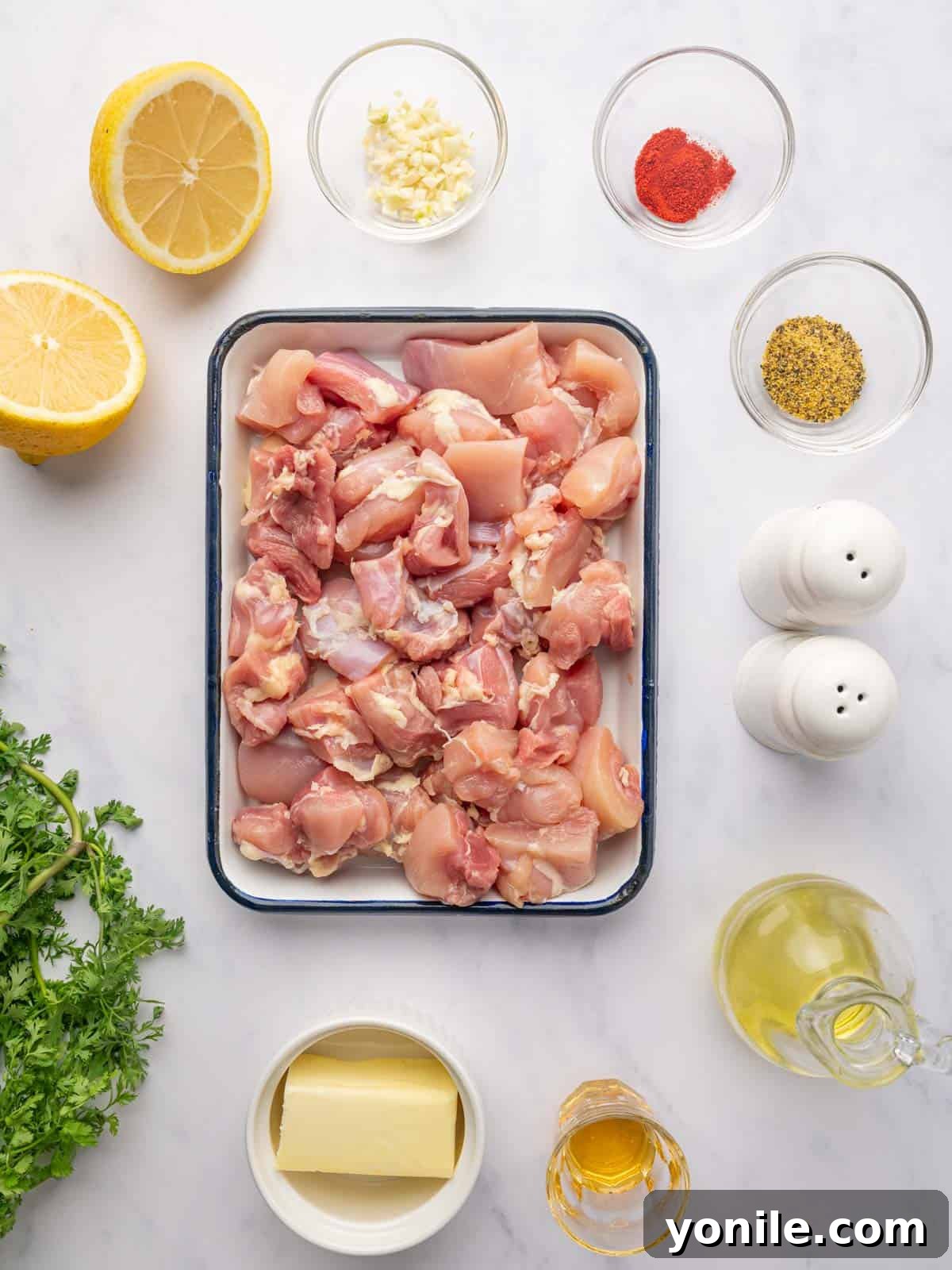 Fresh ingredients laid out for grilled lemon pepper chicken skewers, including lemon, spices, and fresh herbs.