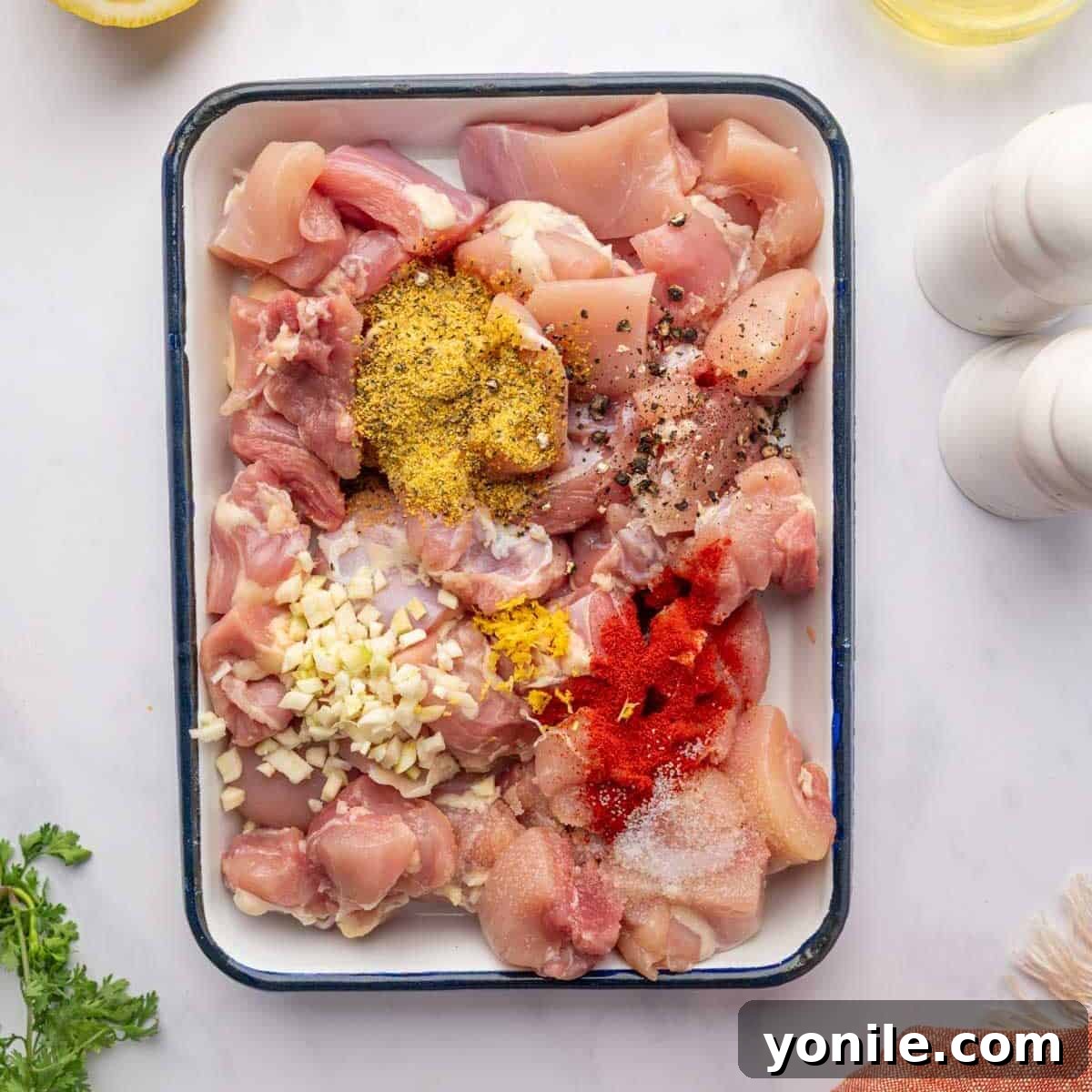 Chicken pieces are mixed with garlic and various seasonings on a tray, preparing for marinade.