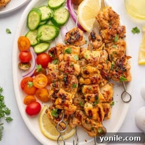 Fresh veggies and lemon wedges surround grilled chicken skewers on a platter, highlighting the complete dish.