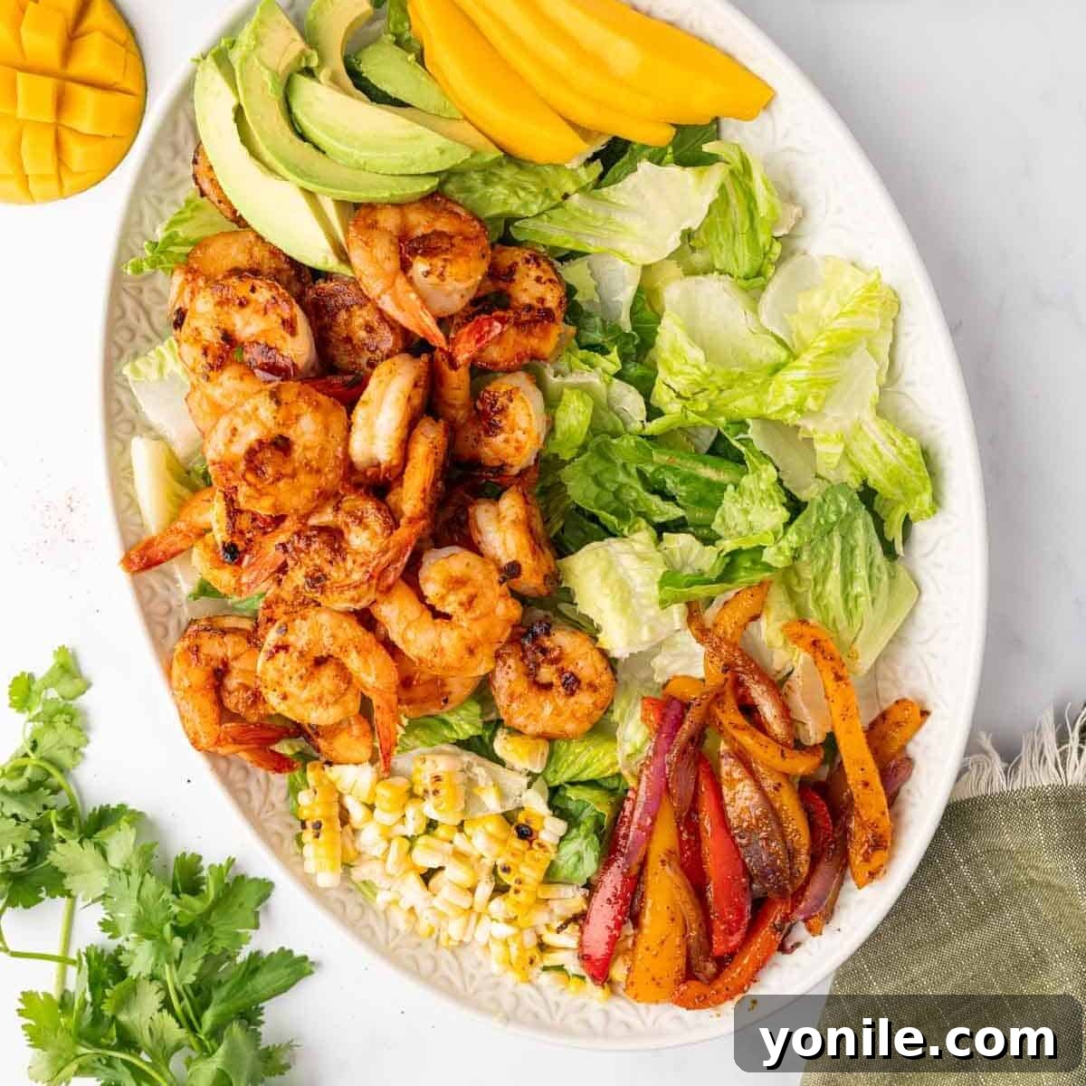 A platter with various ingredients for shrimp salad, including grilled bell peppers, onions, and corn cobs.