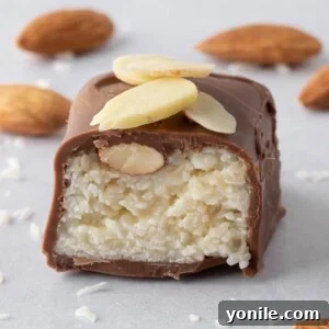 A homemade coconut and almond filled candy bar is cut in half so you can see the creamy, textured filling, showcasing its delicious interior.
