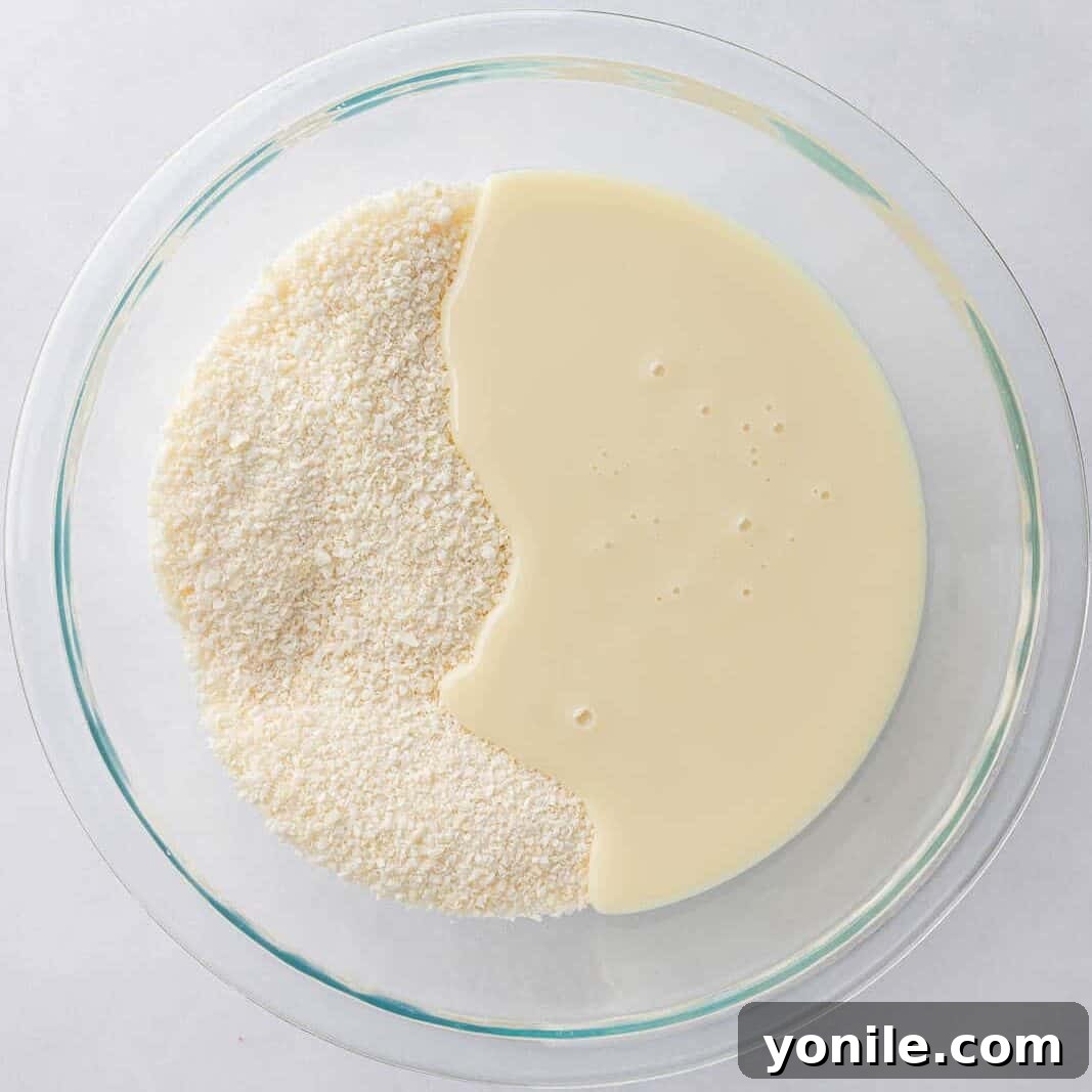 Close-up shot of shredded coconut and sweetened condensed milk being mixed in a bowl, the first step in creating the creamy filling for no-bake candy bars.