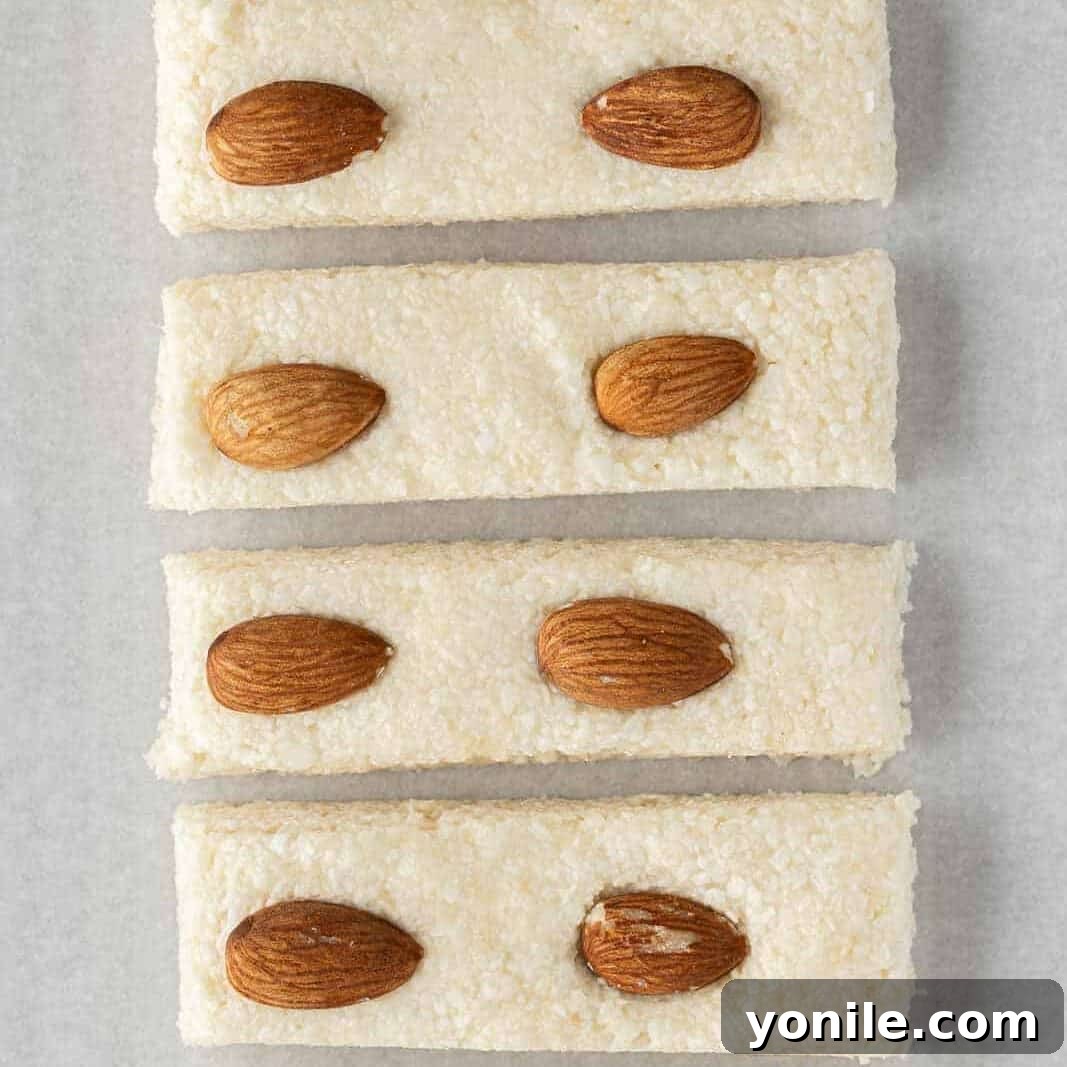 The firm, chilled candy bar filling is carefully cut into individual uniform bars on a cutting board, preparing them for the chocolate coating stage.