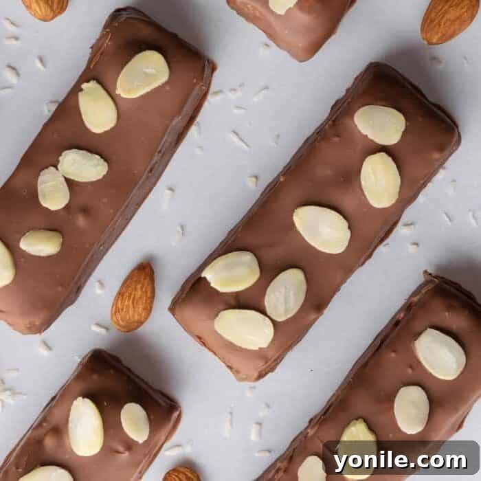 Freshly dipped coconut chocolate bars are garnished with delicate sliced almonds and placed on a tray, ready to chill until the chocolate fully sets.