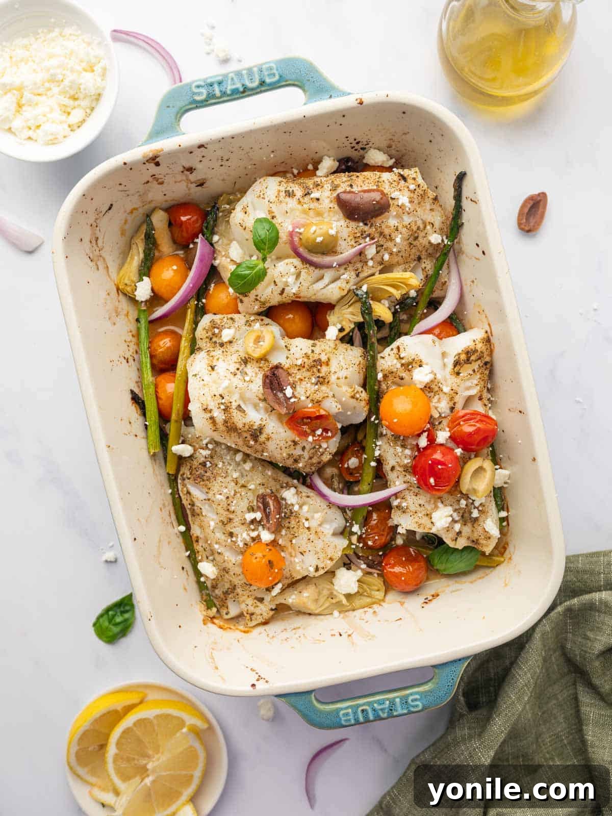 Sun-Kissed Mediterranean Cod 2 Mediterranean cod with roasted vegetables, topped with feta and fresh basil, in a baking dish.