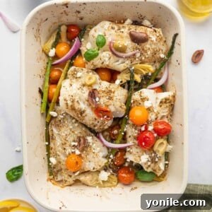 Seasoned cod fish in a rectangle baking dish with asparagus, tomatoes and onions.