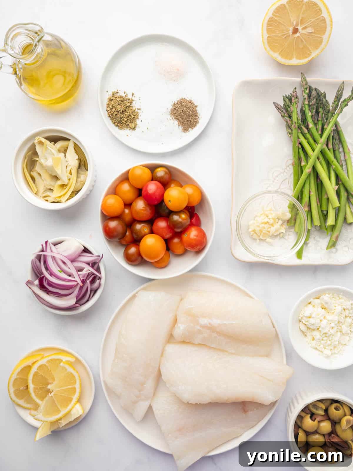 Sun-Kissed Mediterranean Cod 3 Ingredients for Mediterranean cod laid out: cod fillets, cherry tomatoes, asparagus, olives, red onion, artichoke hearts, feta, olive oil, and Greek seasoning.