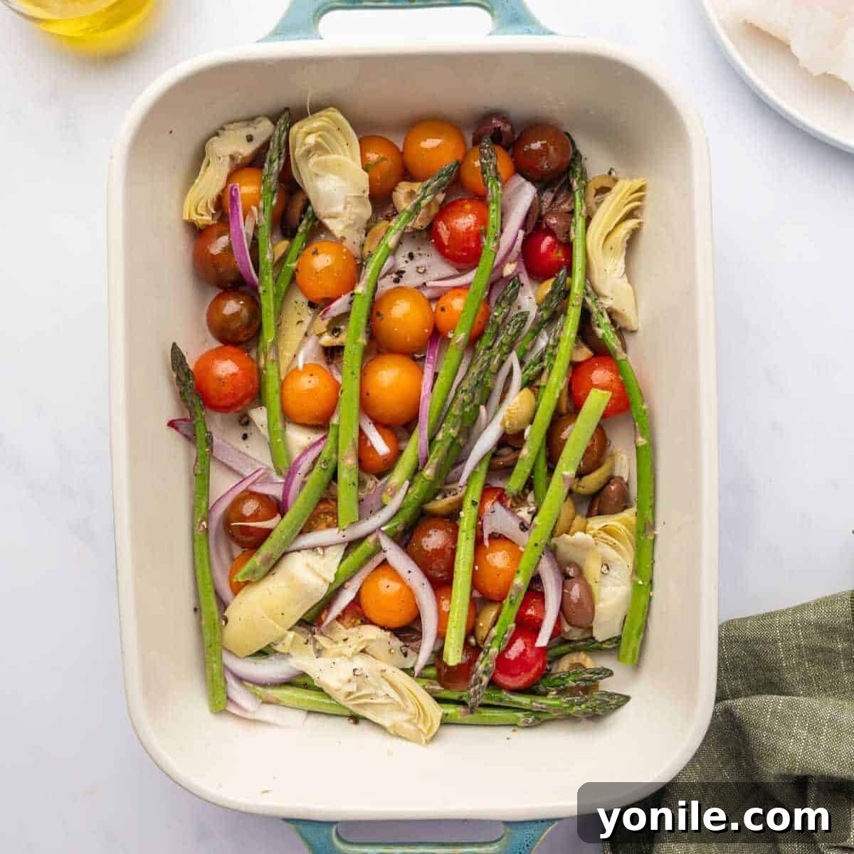 Sun-Kissed Mediterranean Cod 5 Fresh vegetables, including cherry tomatoes, asparagus, and red onion, layered in a baking dish.