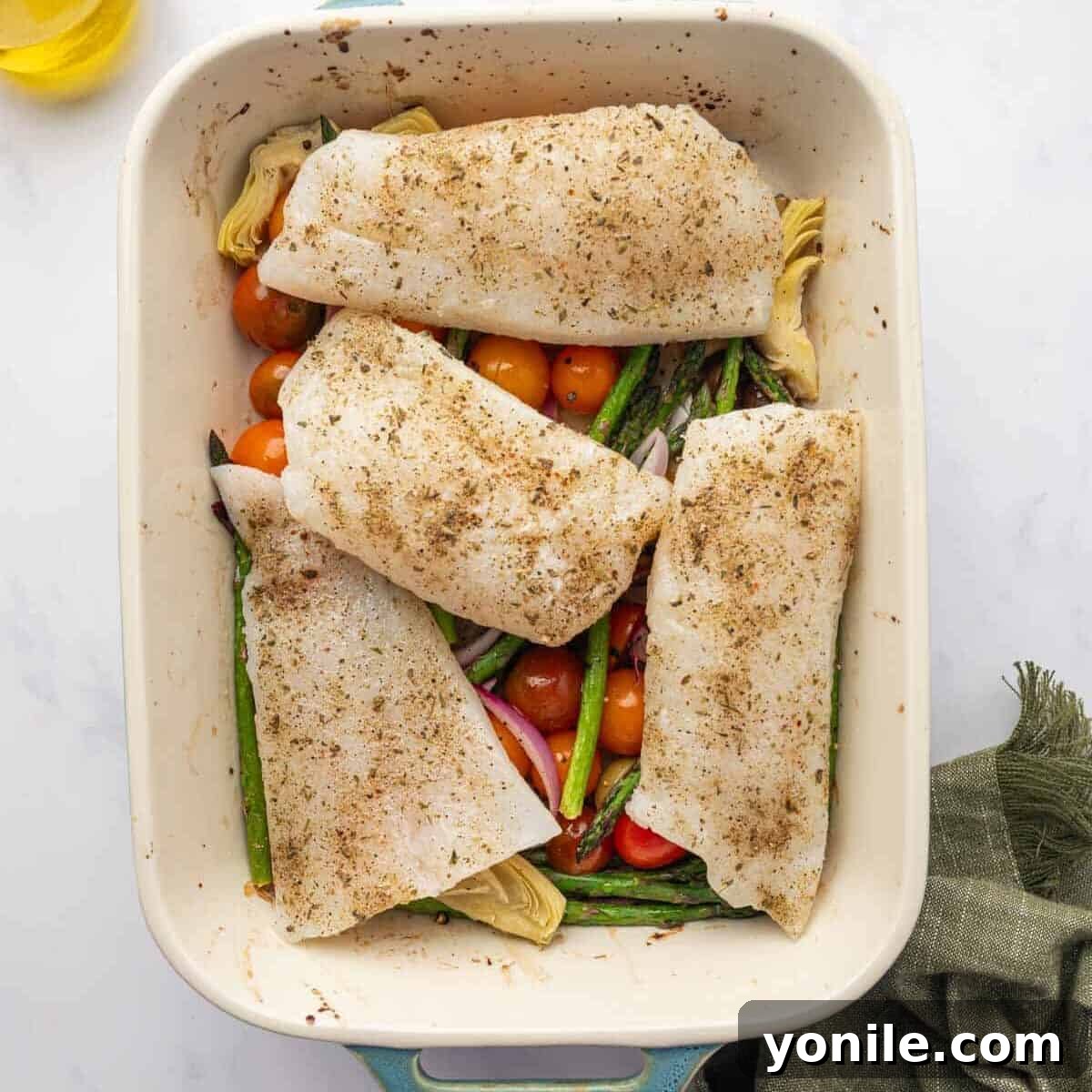 Sun-Kissed Mediterranean Cod 6 Seasoned cod fillets placed on top of roasted vegetables in a baking dish.
