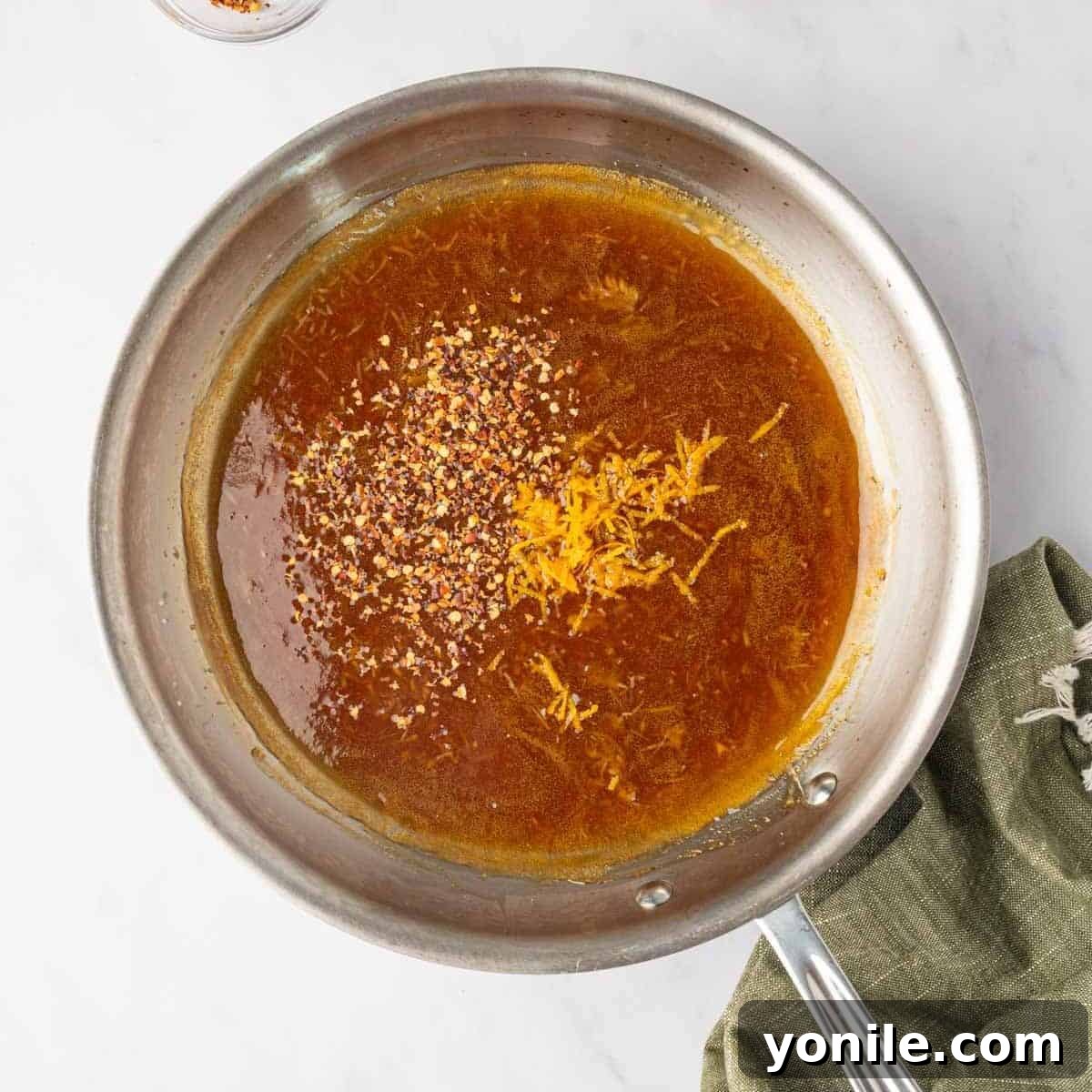 Orange zest is carefully added to the simmering sauce in a skillet, just before removing from heat.
