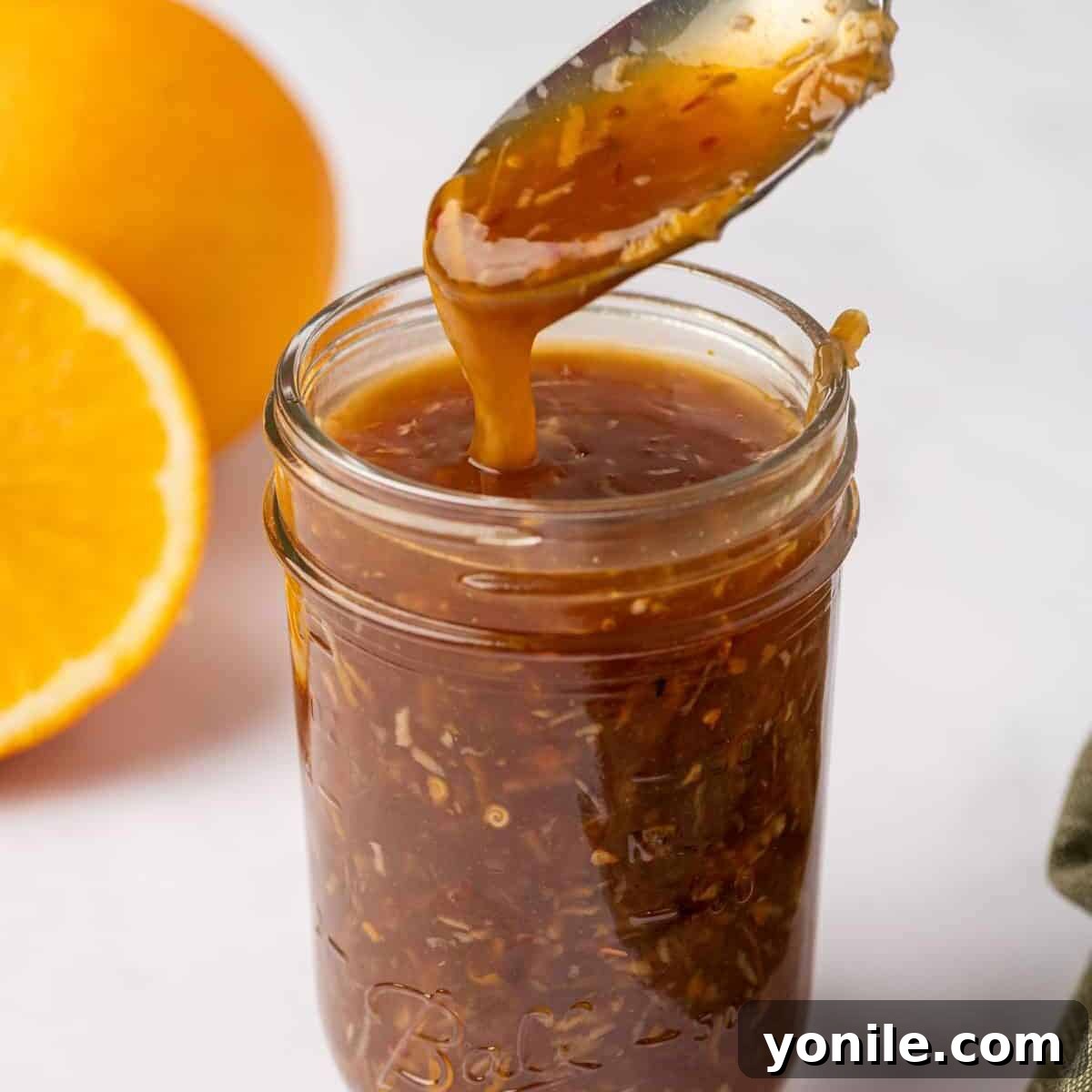 A spoon scoops rich orange chicken sauce from a small glass jar, ready for serving or storage.