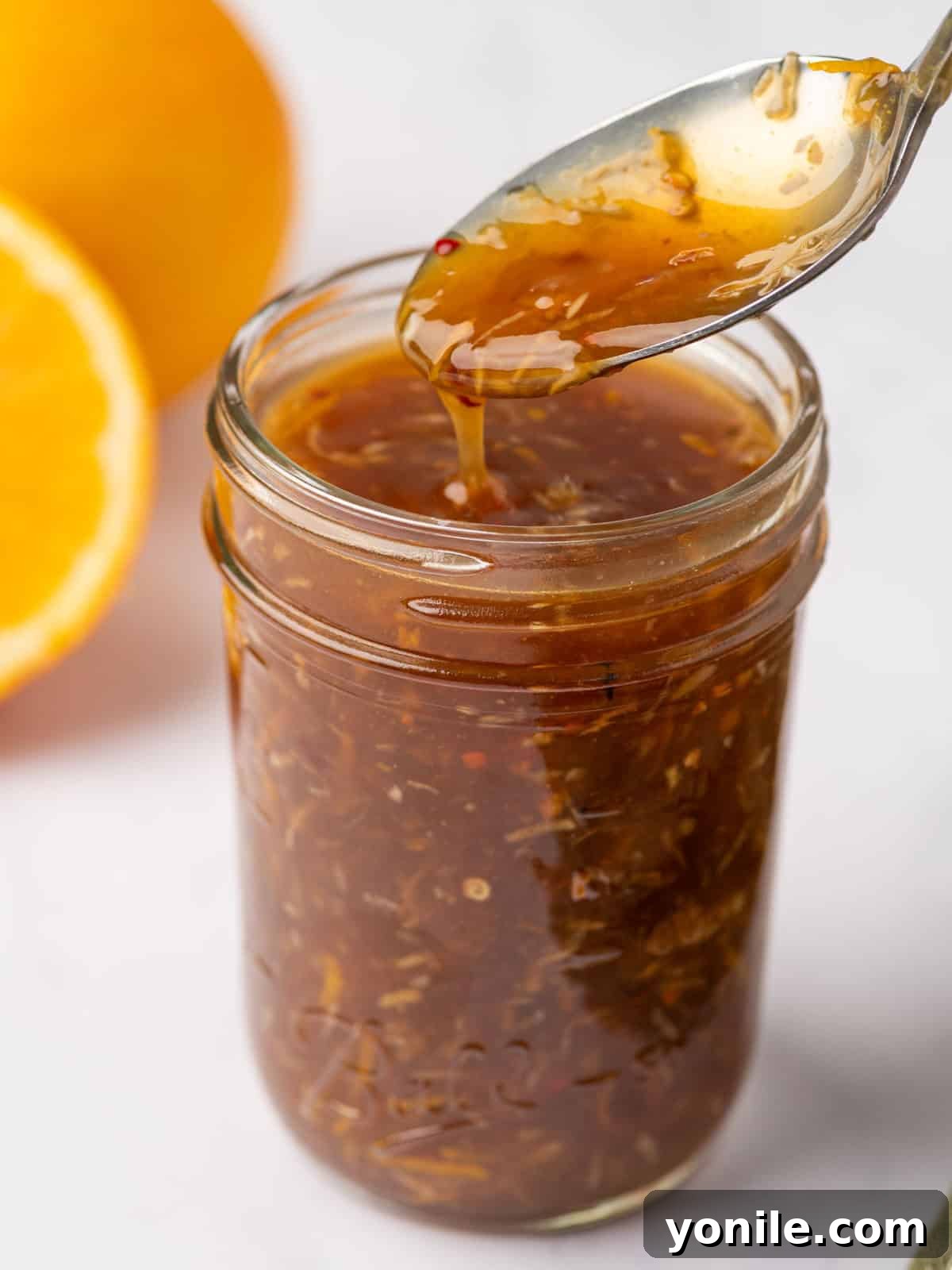 A spoon elegantly dips into a jar of rich homemade orange chicken sauce, ready to be spread or drizzled.