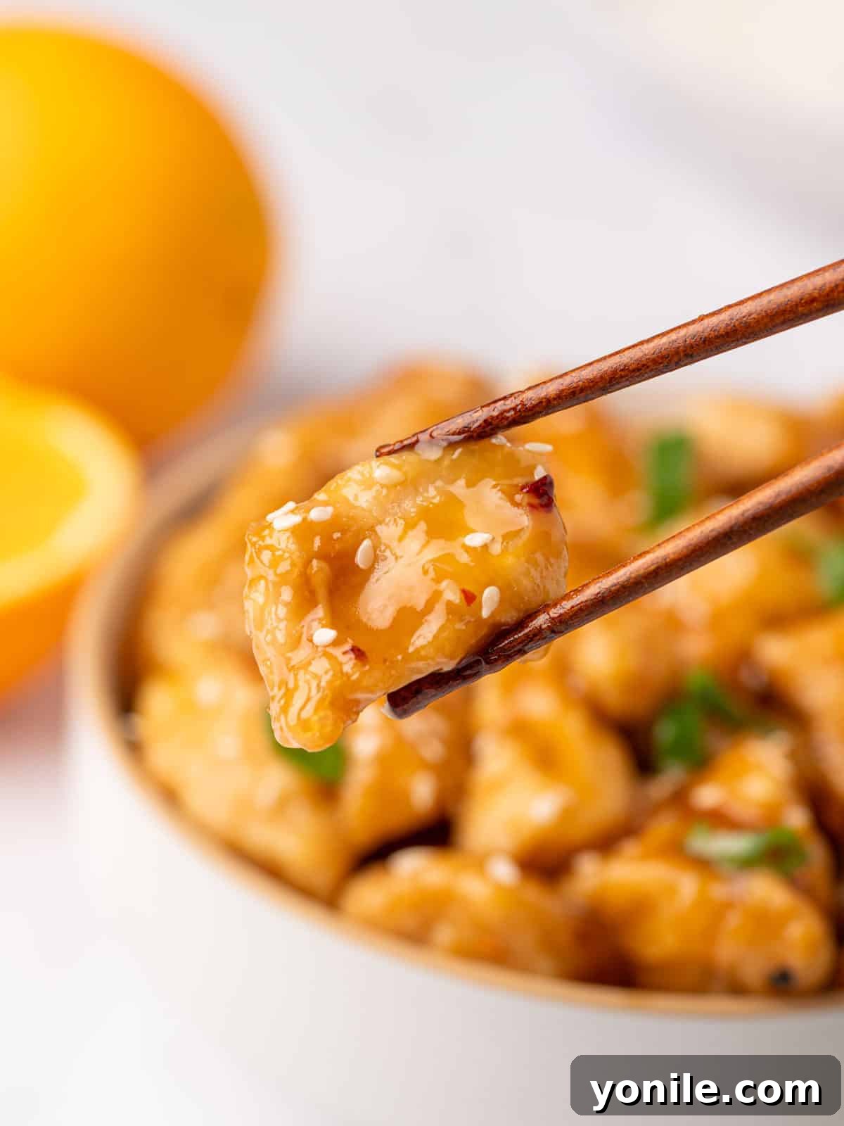 Chopsticks skillfully pick up a piece of golden-fried chicken, glistening with homemade orange sauce.