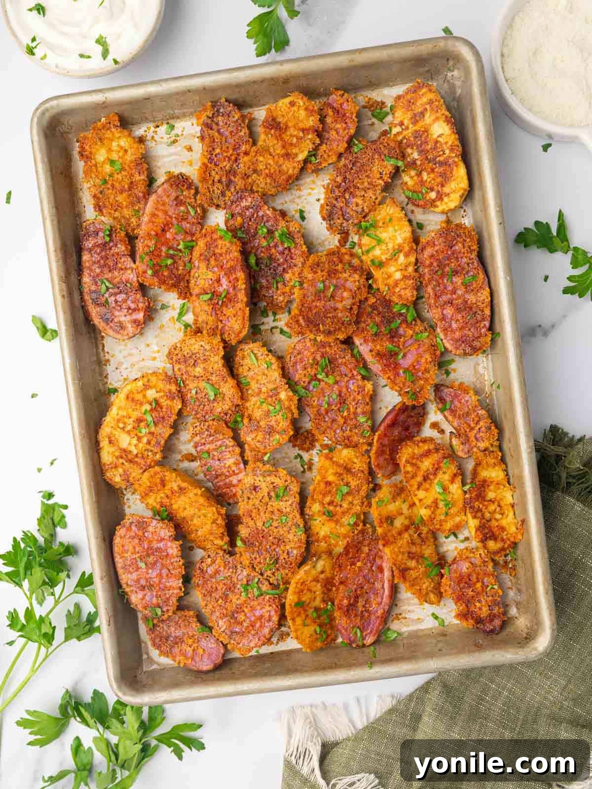A baking tray filled with golden-brown cheesy roasted fingerling potatoes, garnished with fresh green parsley.