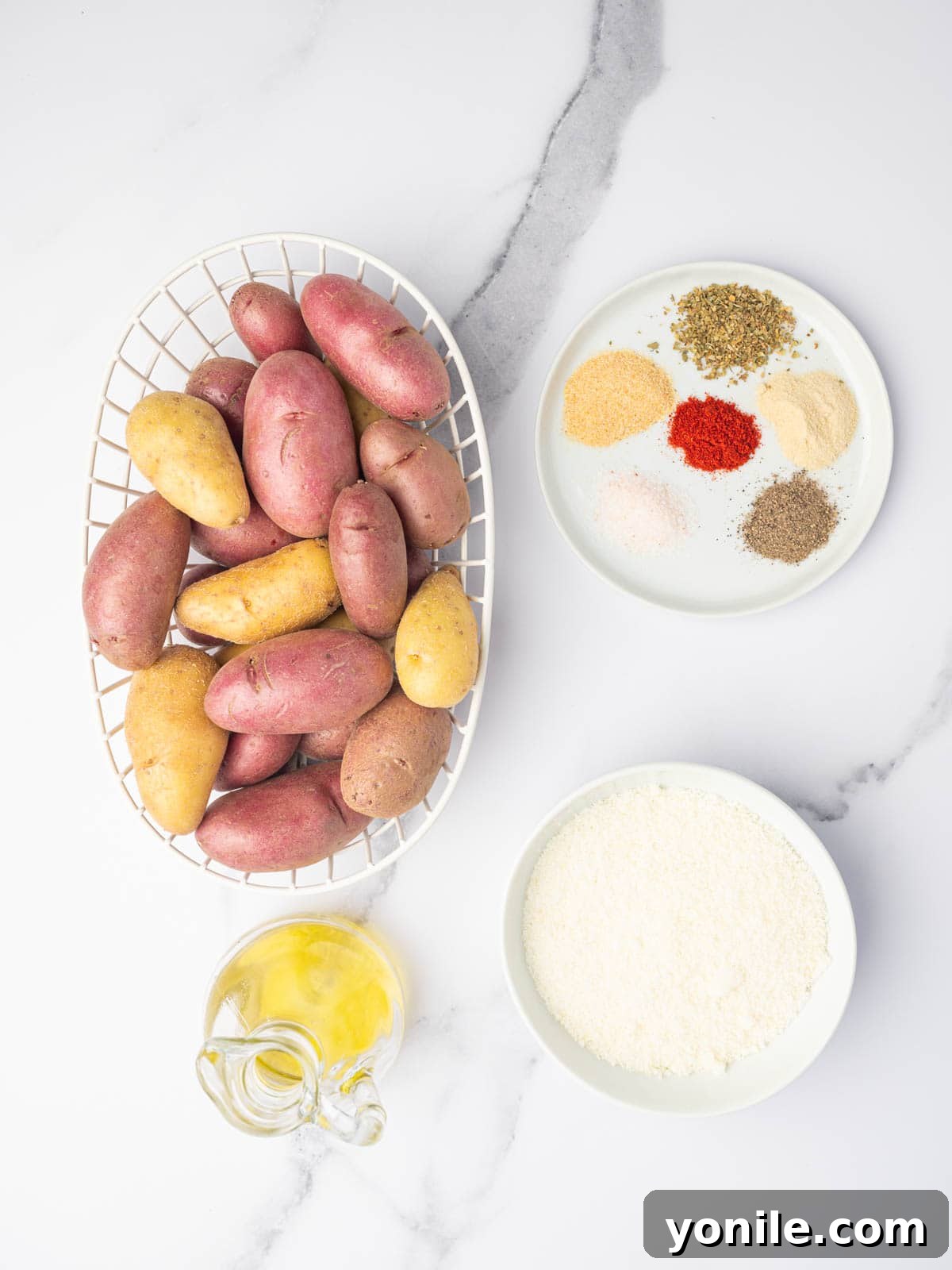 A flat lay photograph showcasing the ingredients required to prepare cheesy roasted fingerling potatoes, including potatoes, olive oil, parmesan cheese, and various spices.