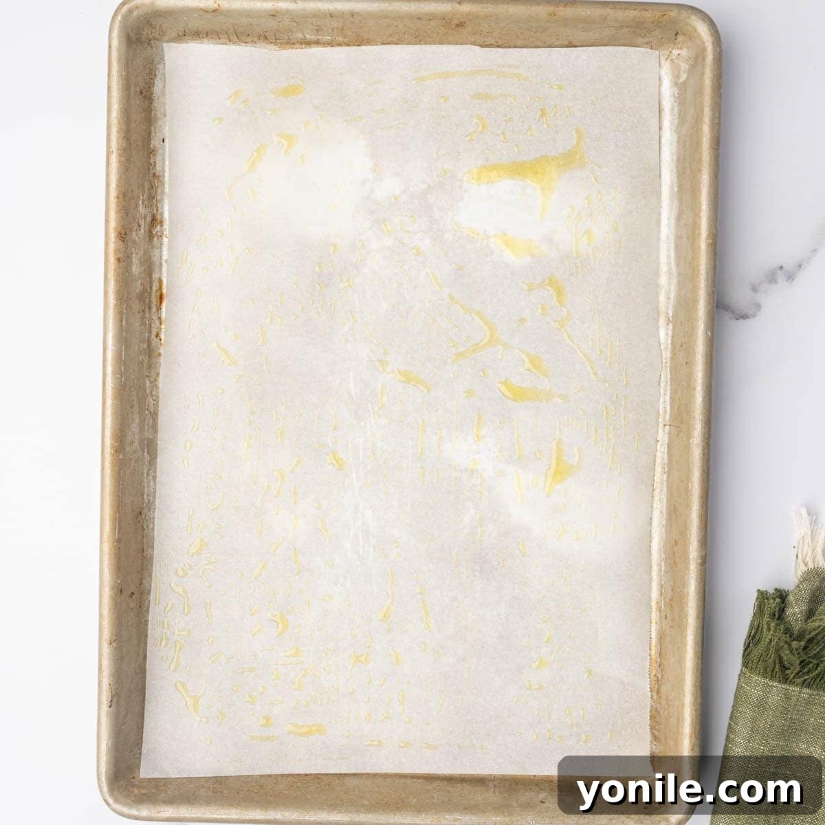 A baking sheet lined with parchment paper, glistening with a drizzle of olive oil, ready for the cheese and potatoes.