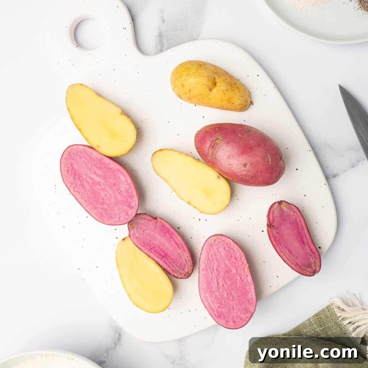 Fingerling potatoes, freshly washed and dried, are meticulously sliced in half lengthwise on a cutting board, showcasing their creamy interior.