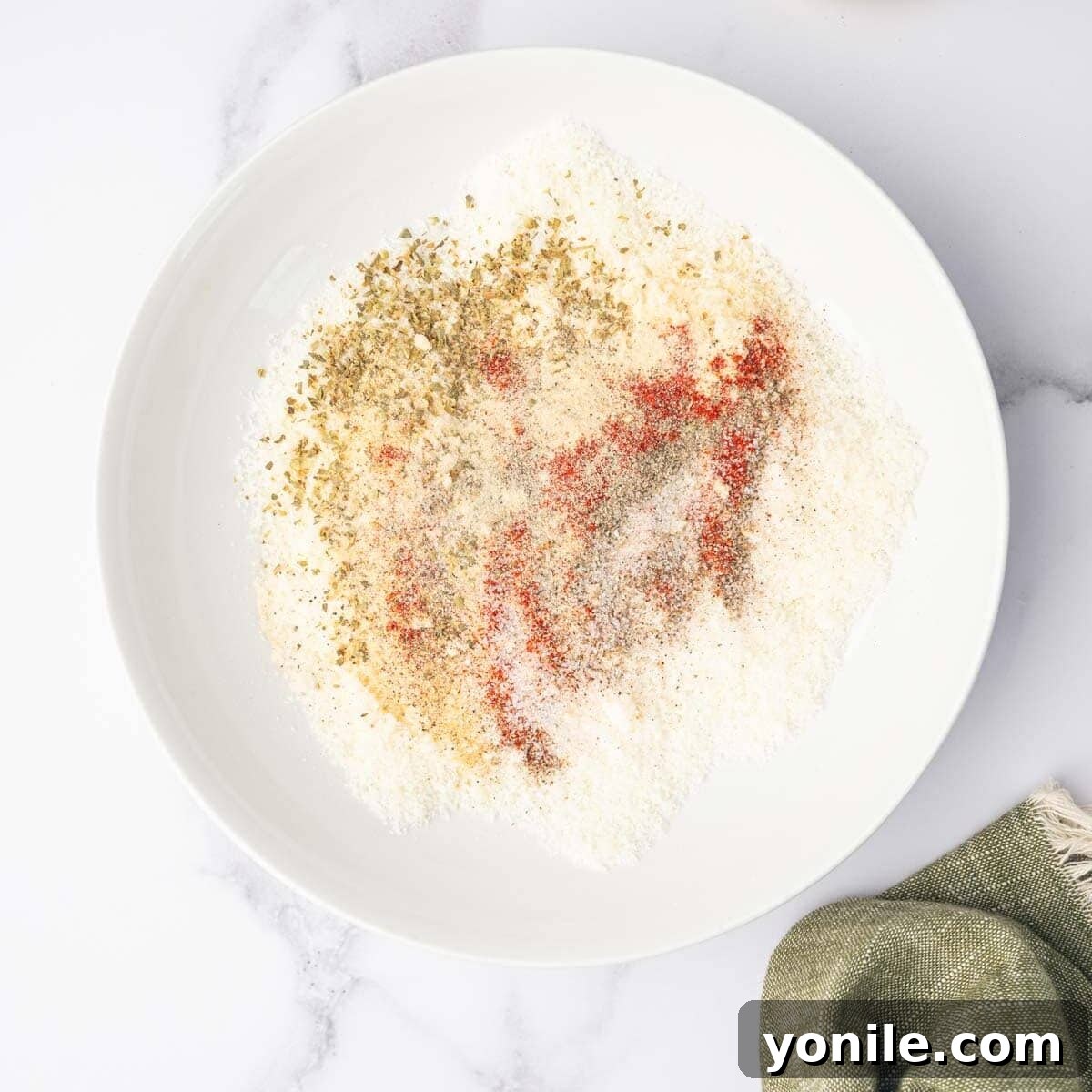 A small glass bowl containing a vibrant mixture of grated Parmesan cheese and various dried spices, ready to be spread.