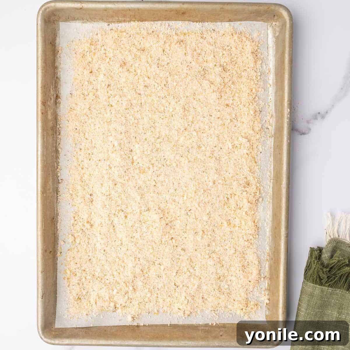 A uniform layer of the Parmesan cheese and spice mixture is carefully spread over the olive oil-drizzled parchment paper on a baking sheet, creating the base for the potatoes.