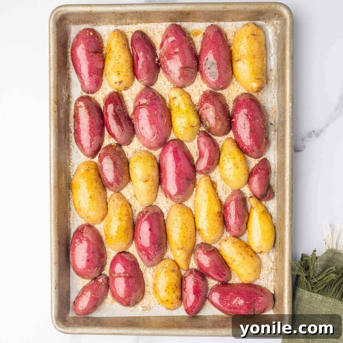 Oil-coated fingerling potato halves are carefully arranged, cut-side down, directly onto the bed of Parmesan and spices on the baking sheet.