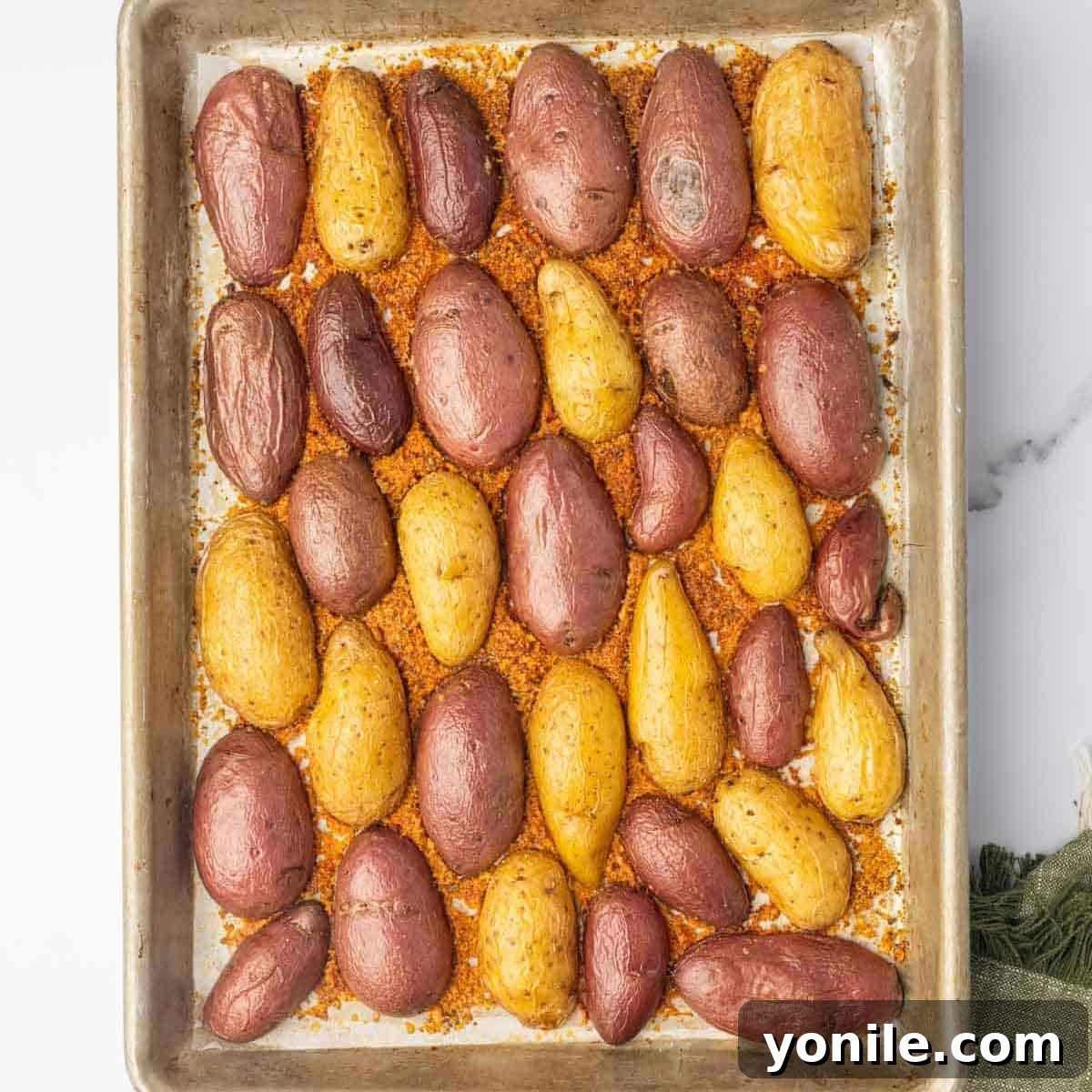 The baking sheet, laden with neatly arranged fingerling potatoes on their cheesy base, slides into a preheated oven for roasting.