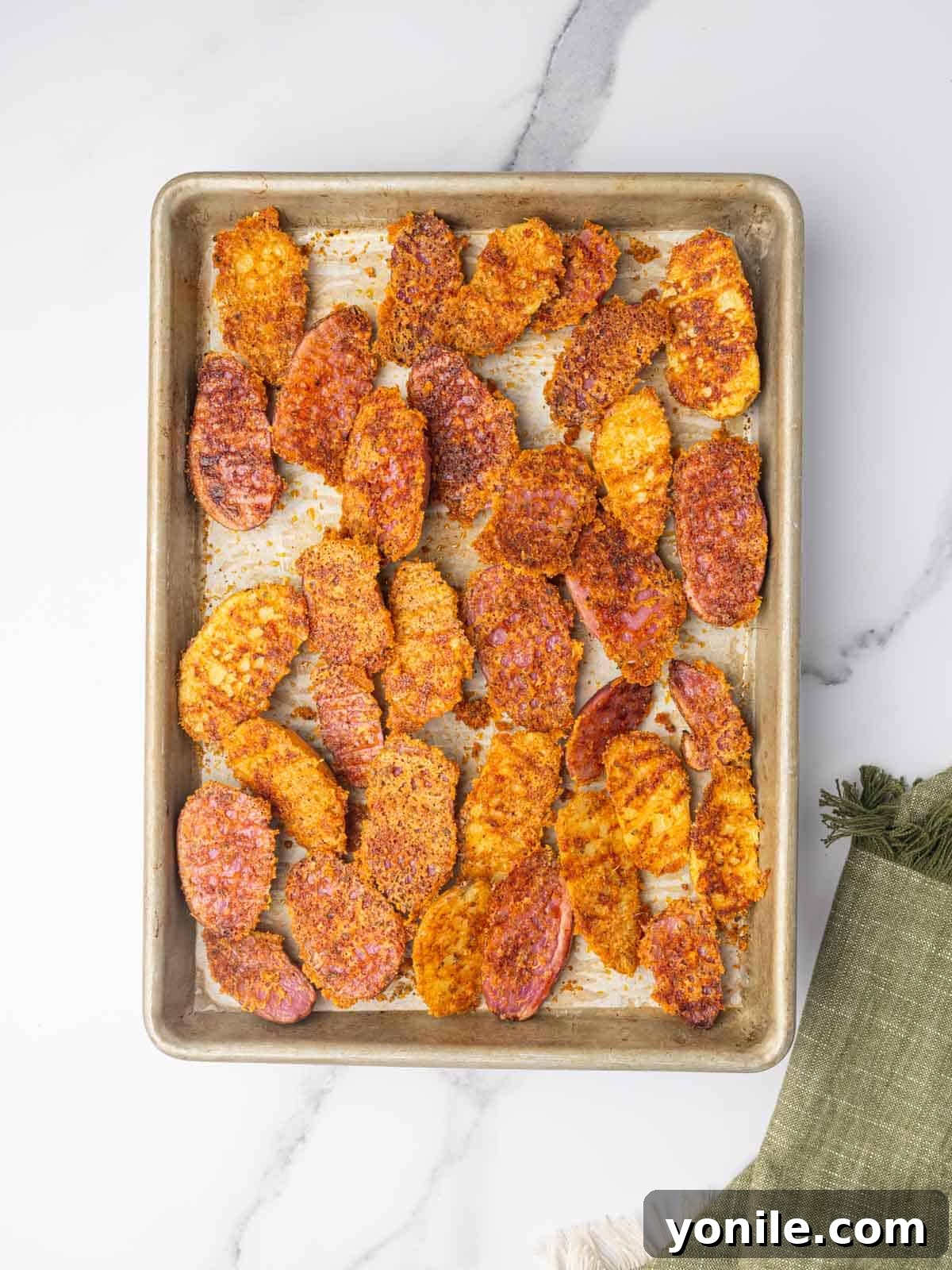 A close-up view of roasted fingerling potatoes still on the baking tray, showcasing their perfect crispy cheese crust and tender appearance.