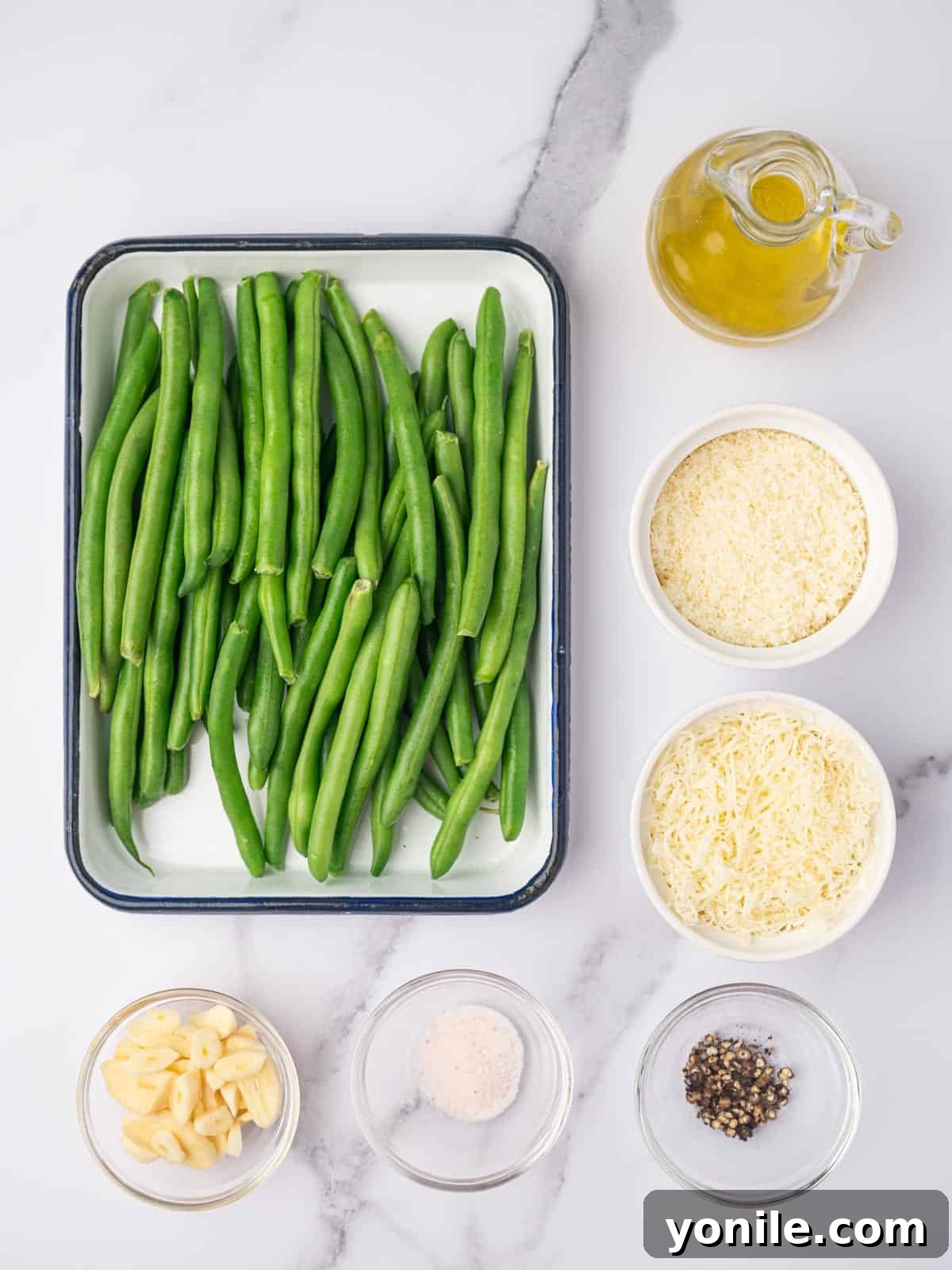 Fresh green beans, olive oil, garlic, salt, pepper, and two types of cheese laid out as ingredients for baked green beans.