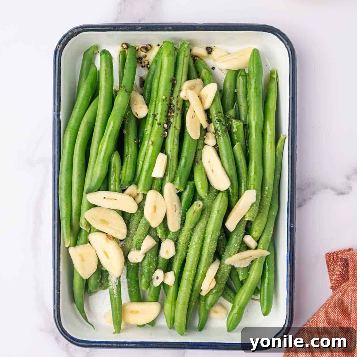 A tray of fresh green beans mixed with sliced garlic and spices, ready for baking.