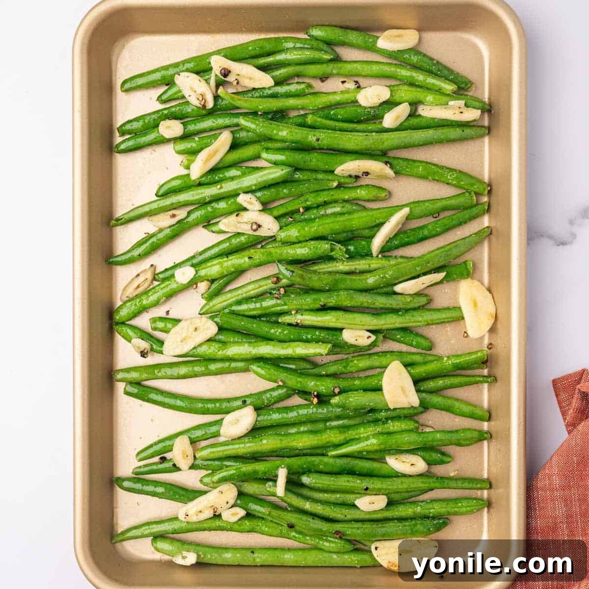 Seasoned green beans are layered evenly on a baking sheet, ready for the oven.