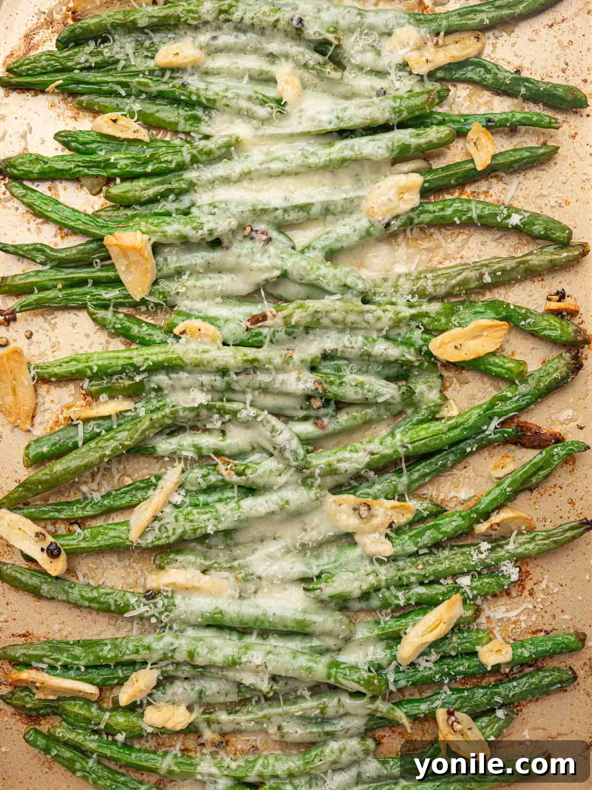 A tray of green beans baked with garlic and parmesan cheese, garnished with fresh herbs.