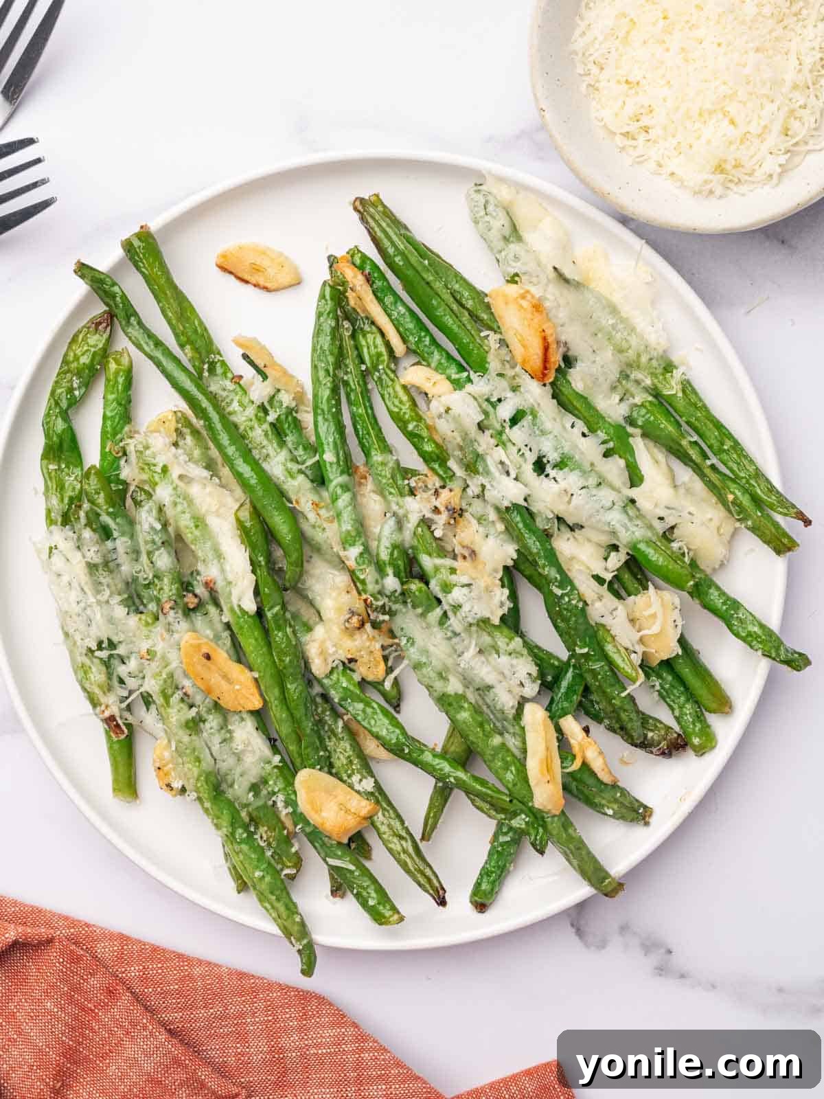 A round white serving plate with parmesan covered green beans, ready to be enjoyed.