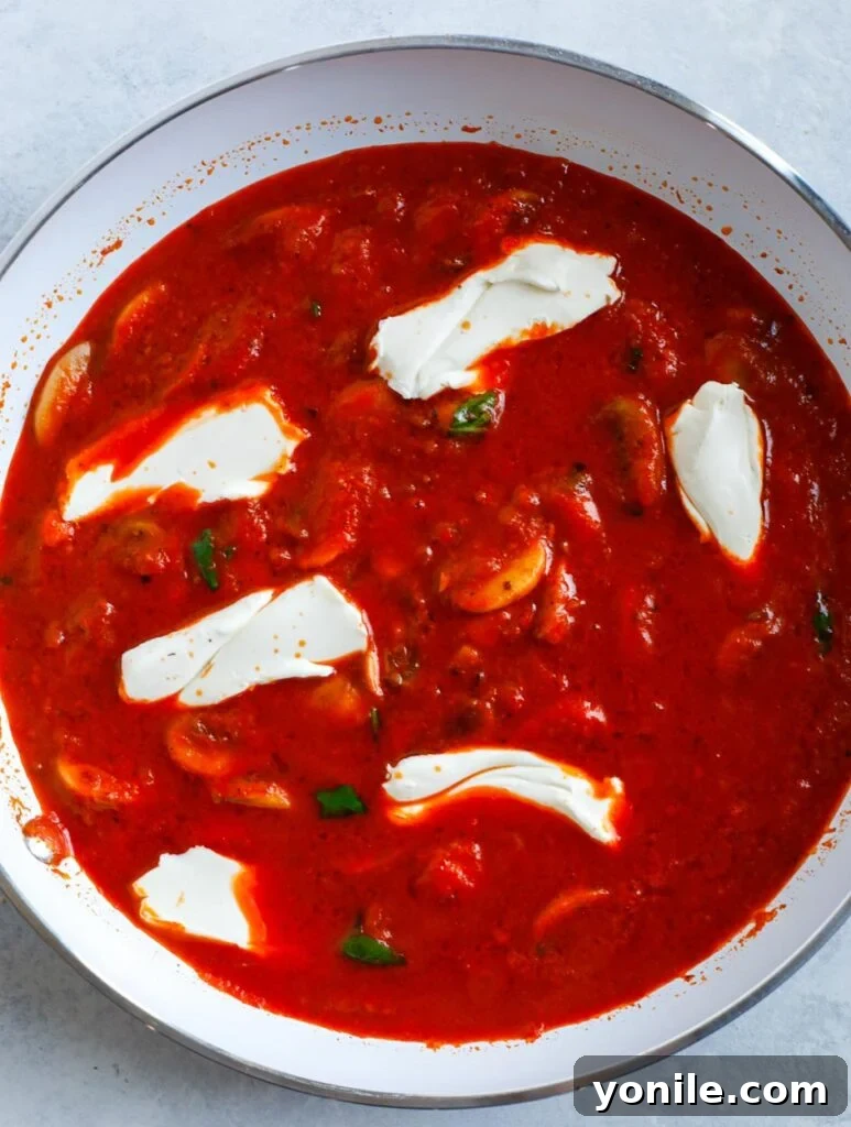 Cream cheese melting into a red pepper pasta sauce in a skillet