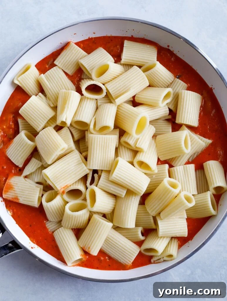 Cooked rigatoni pasta tossed in creamy red pepper sauce in a skillet