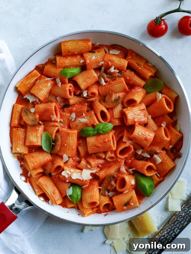 Top-down shot of creamy red pepper rigatoni pasta in a bowl with fresh basil garnish