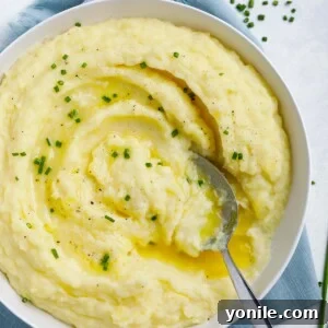 Effortless Velvety Mash 5 creamy mashed potatoes in a white plate topped with melted butter and chives, with a spoon in the plate