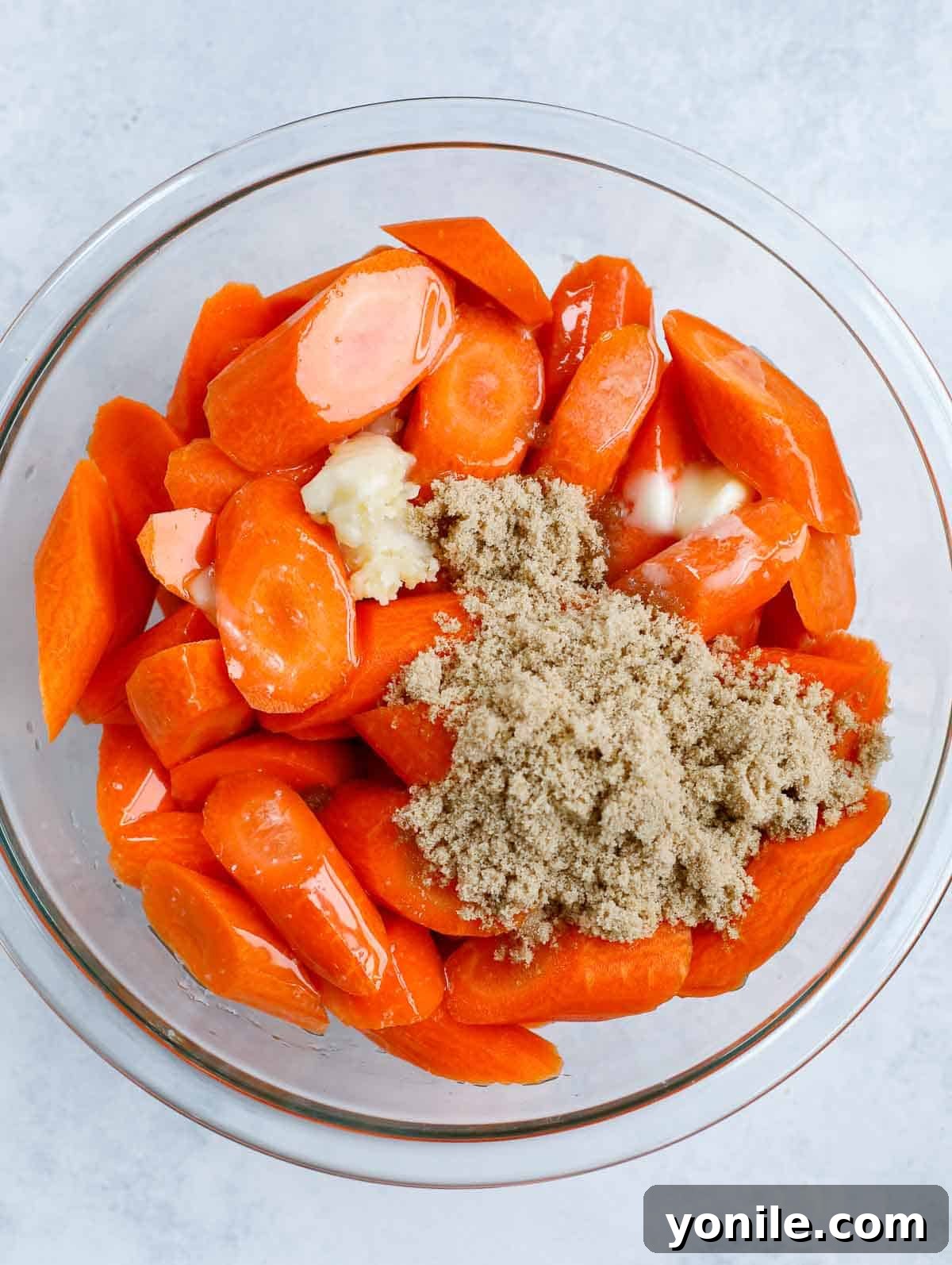 brown sugar glazed carrots in a clear bowl before mixing ingredients together, showing carrots and the glaze mixture