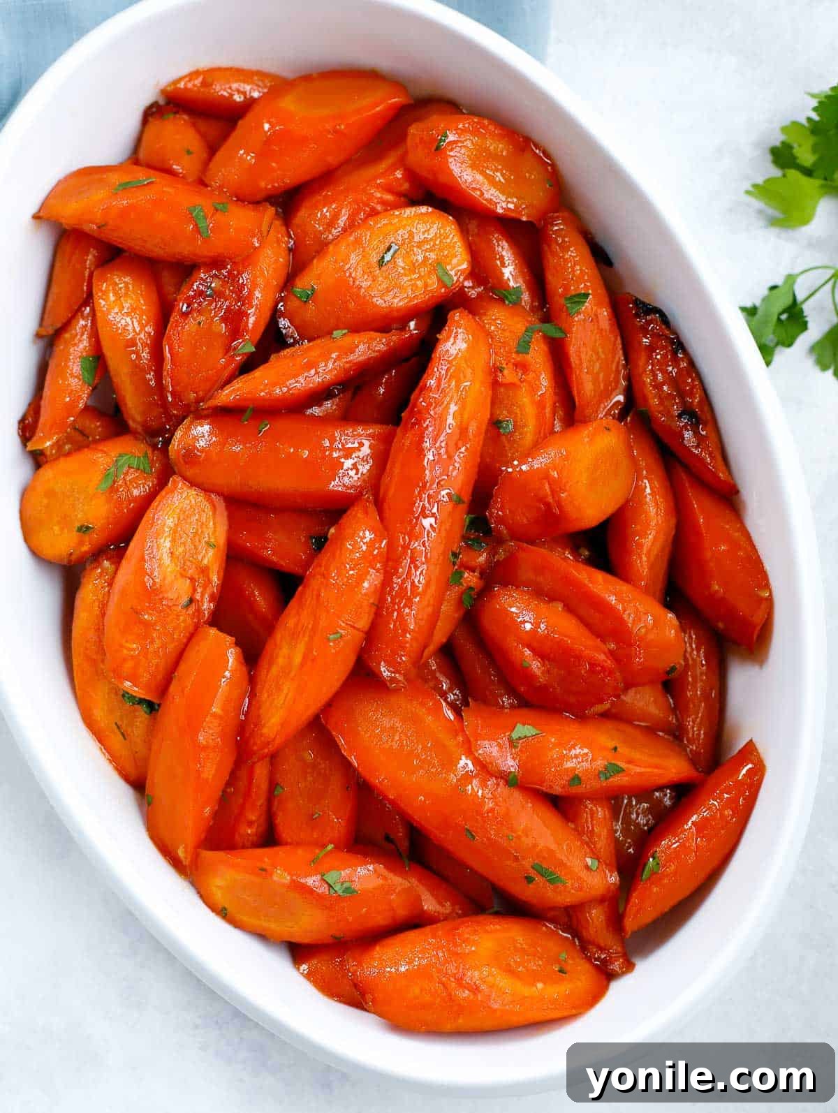 brown sugar glazed carrots on a white serving dish with fresh parsley garnish