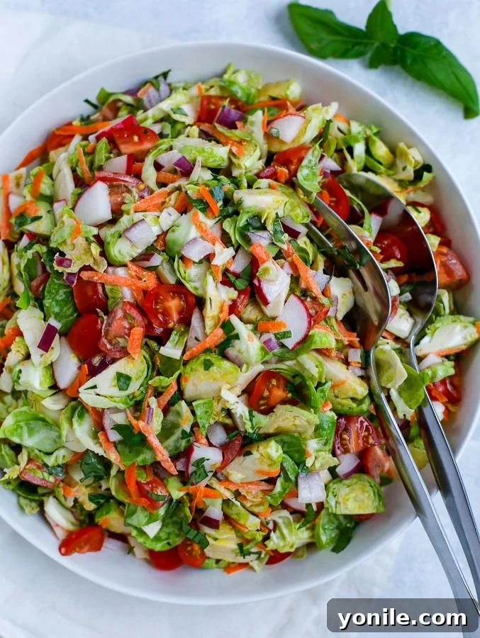 A vibrant raw Brussels sprouts salad in a pristine white bowl, showcasing shredded greens and colorful vegetables, topped with a creamy dressing.