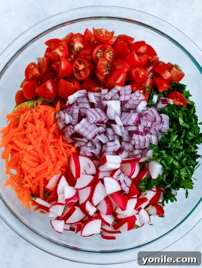 A colorful array of chopped vegetables, including shredded Brussels sprouts, tomatoes, and carrots, mixed in a large bowl.