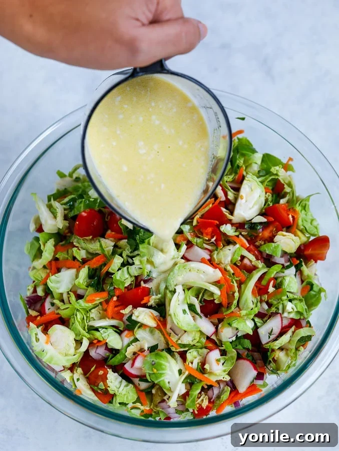 A creamy lemon mayo dressing being poured over a bowl of mixed shredded Brussels sprouts and fresh vegetables.