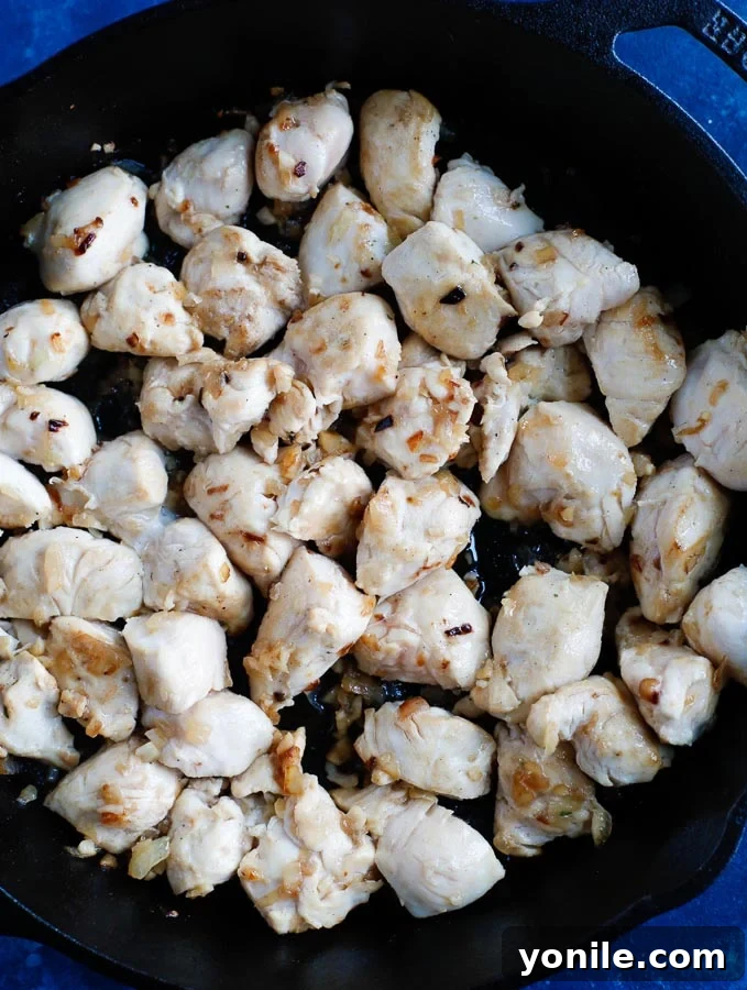 Chicken cubes being sautéed in a skillet, turning golden brown and almost cooked through, ready to be set aside.